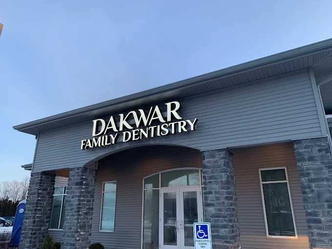 The front of the Dakwar Family Dentistry building: the lit sign over the entrance, stone columns and an accessible parking sign