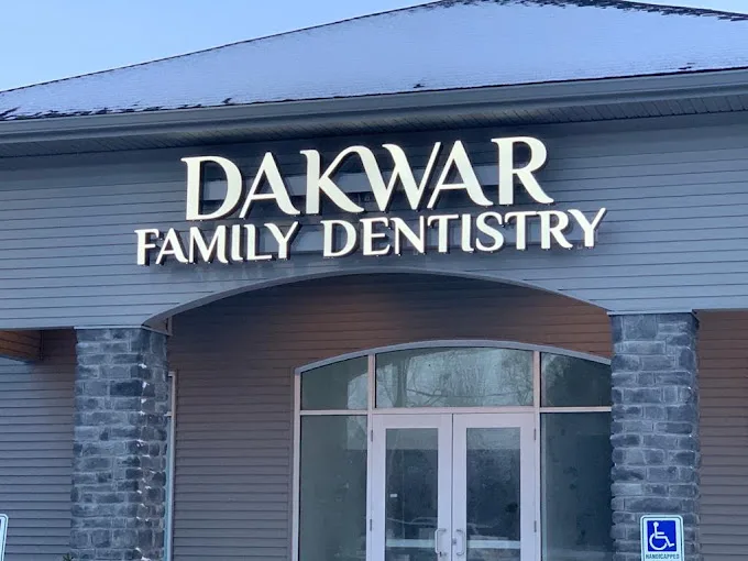 The lit Dakwar Family Dentistry sign over the glass front doors, between two stone columns