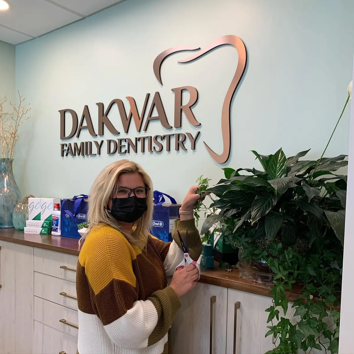 A member of the team trimming the plants at the front desk, under the Dakwar Family Dentistry sign