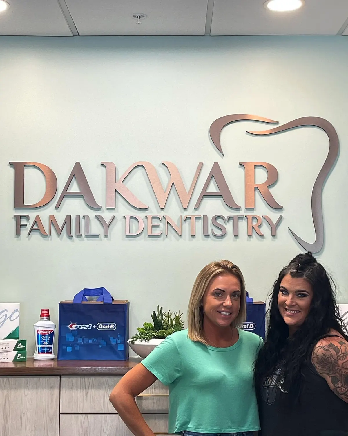 Two smiling women at the front desk, under the copper Dakwar Family Dentistry sign